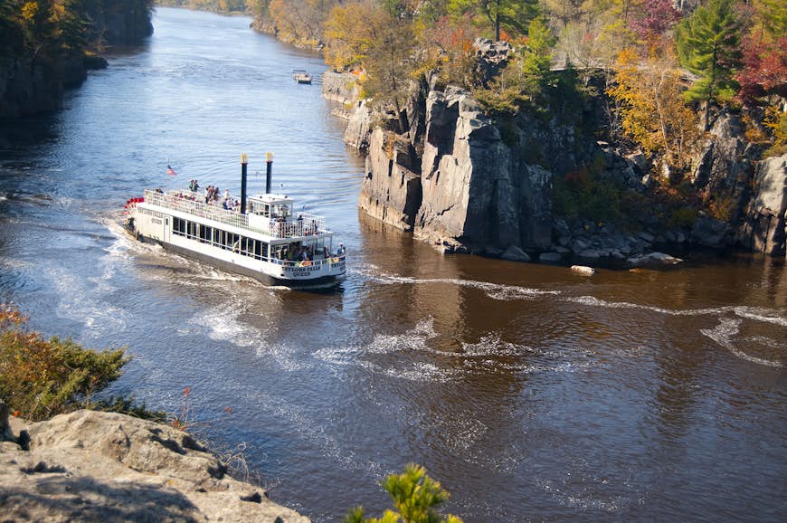 A paddle boat on the St. Croix River in Stillwater, Minnesota, with trees on the rocky riverbanks with leaves of red, orange, gold and green