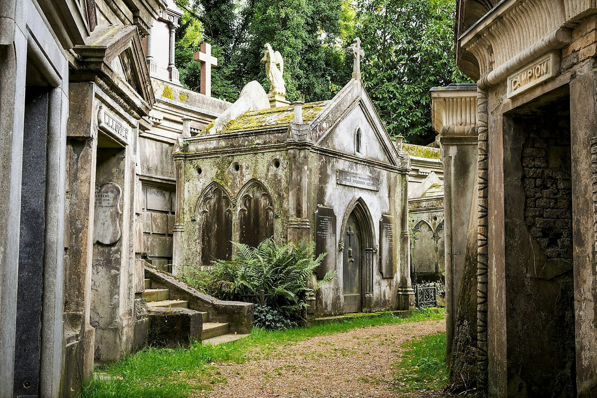 An old moss-covered stone mausoleum sits among a collection of other aging mausoleums in an old cemetery; London  
