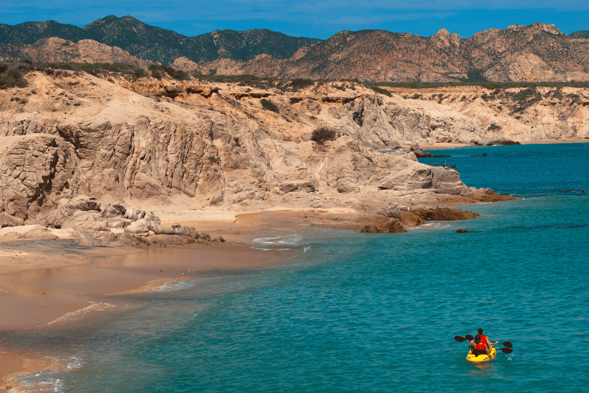 A couple kayaks along an empty beach with red rocks in the background © fitopardo / Getty Images