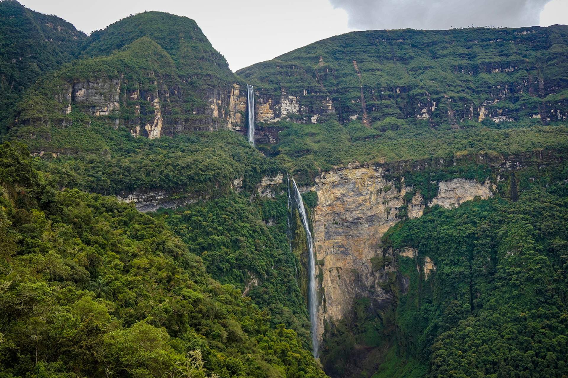 A long skinny waterfall flows down from a two-tiered forested cliff in Northern Peru © Brendan Sainsbury / Lonely Planet