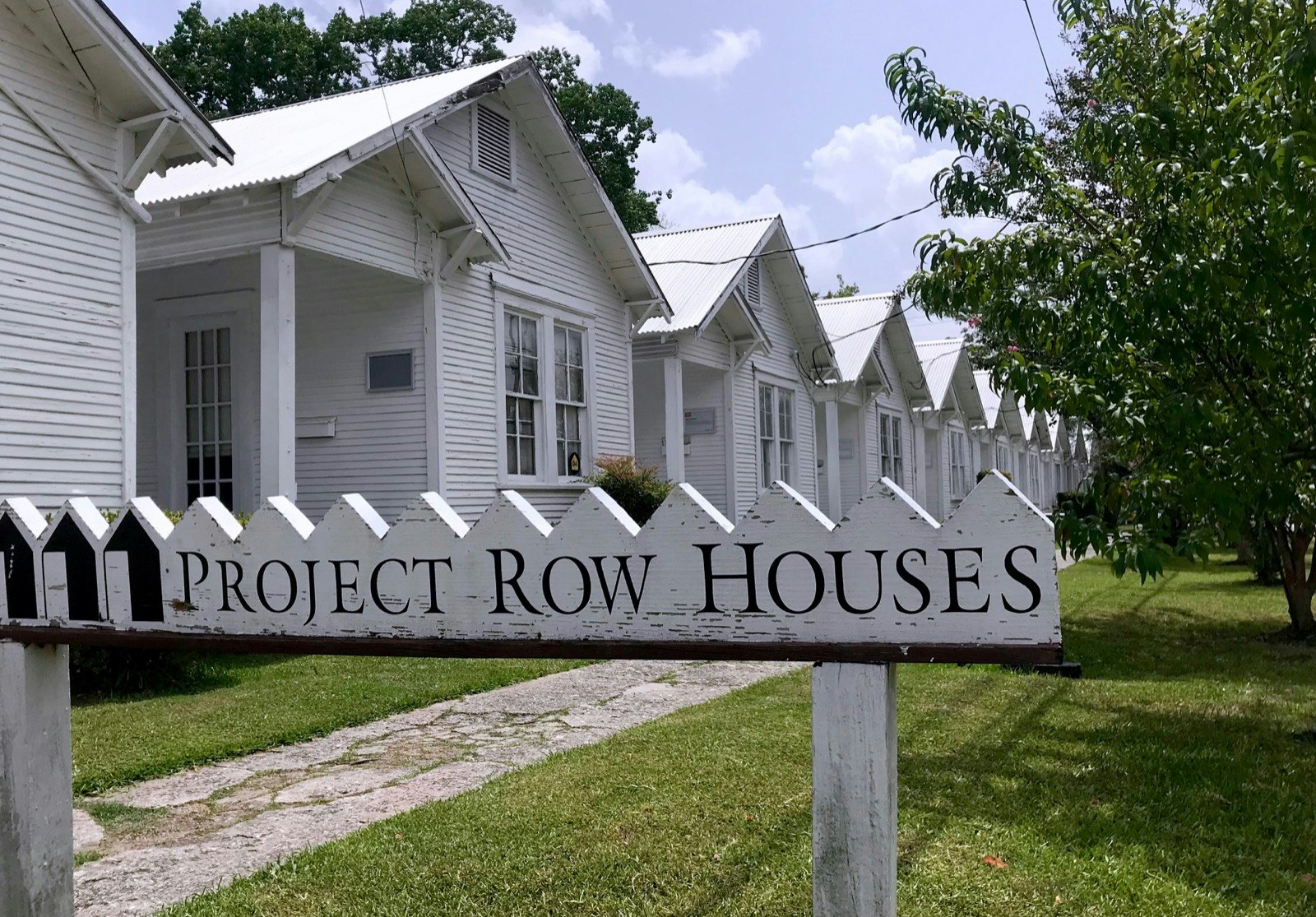 A line of identical small white-painted houses, with a sidewalk in front, is framed by a sign that reads 'Project Row Houses' © Lisa Dunford / Lonely Planet