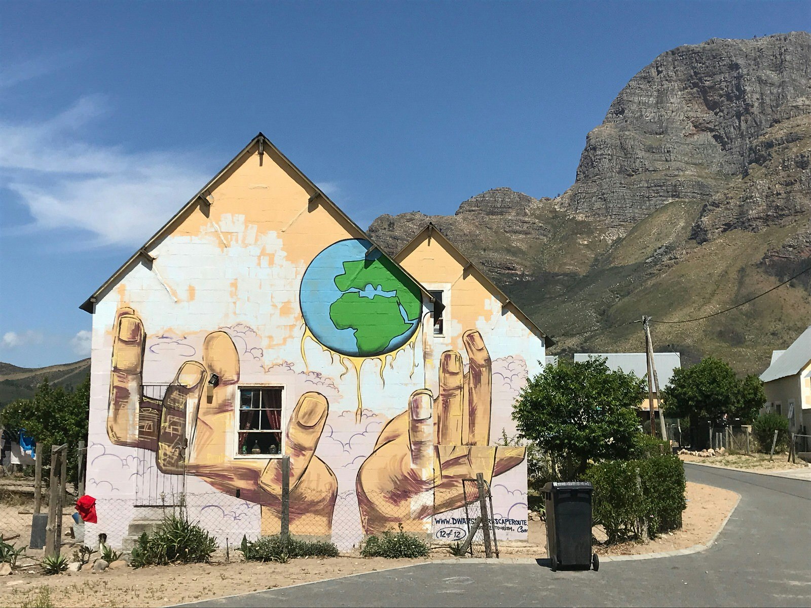 A giant mural of a pair of hands spread across the split facade of a family home, with the rugged majesty of the Drakenstein Mountains in background © Simon Richmond / Lonely Planet