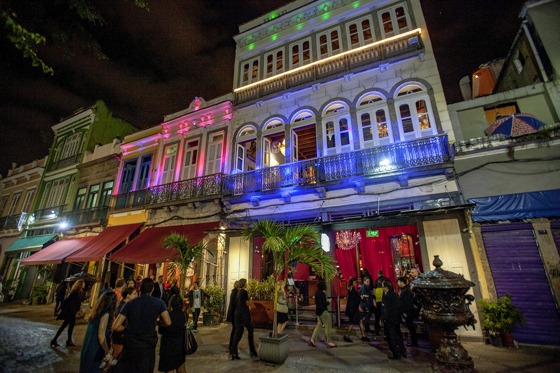 A photo of the colorful facade of Rio Scenarium lit with blue, pink and green lights, as revelers walk towards the front entrance