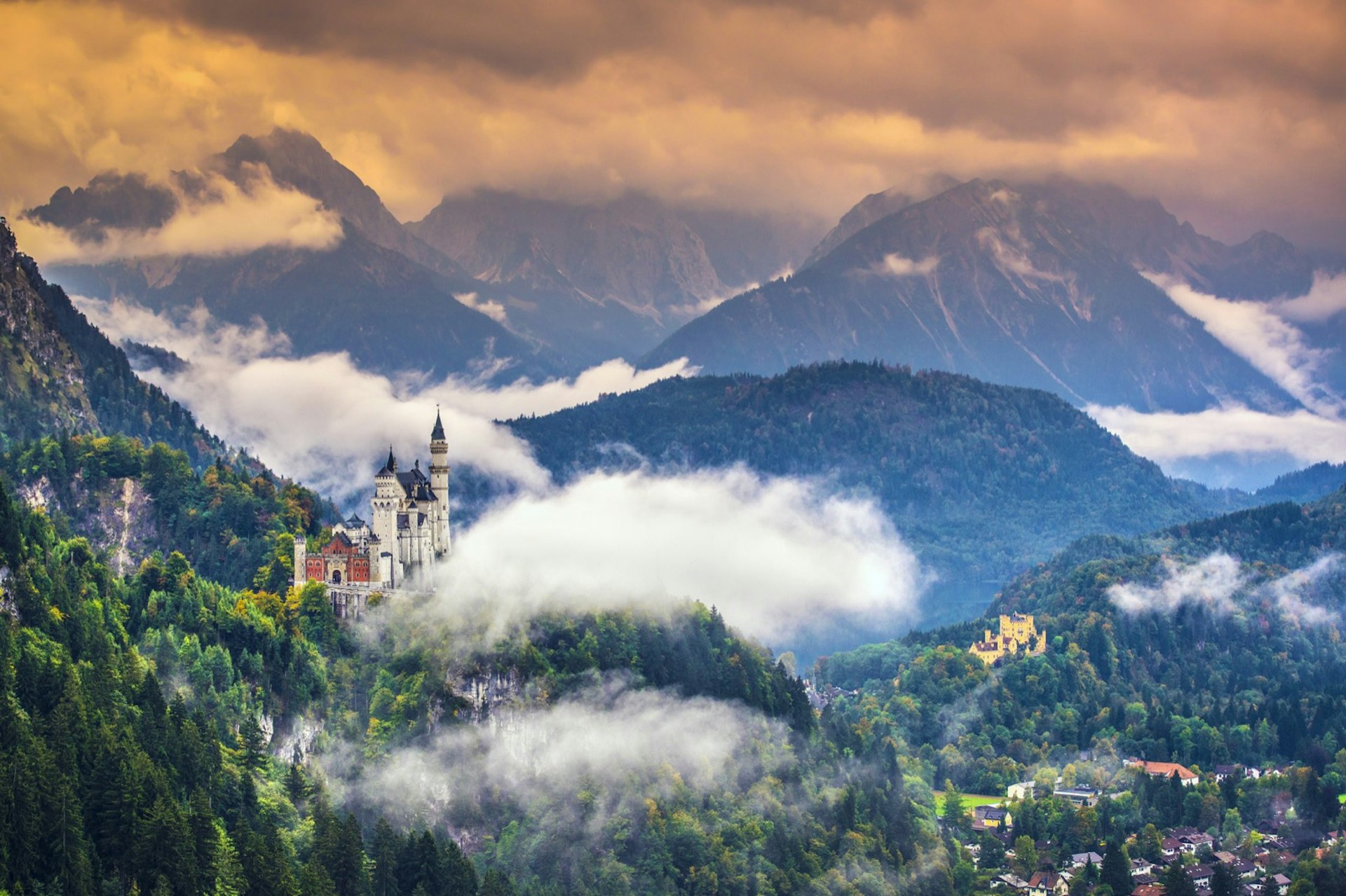 Neschwanstein Castle in the Bavarian Alps of Germany pokes through some clouds as the village is seen far below; Germany for first-timers