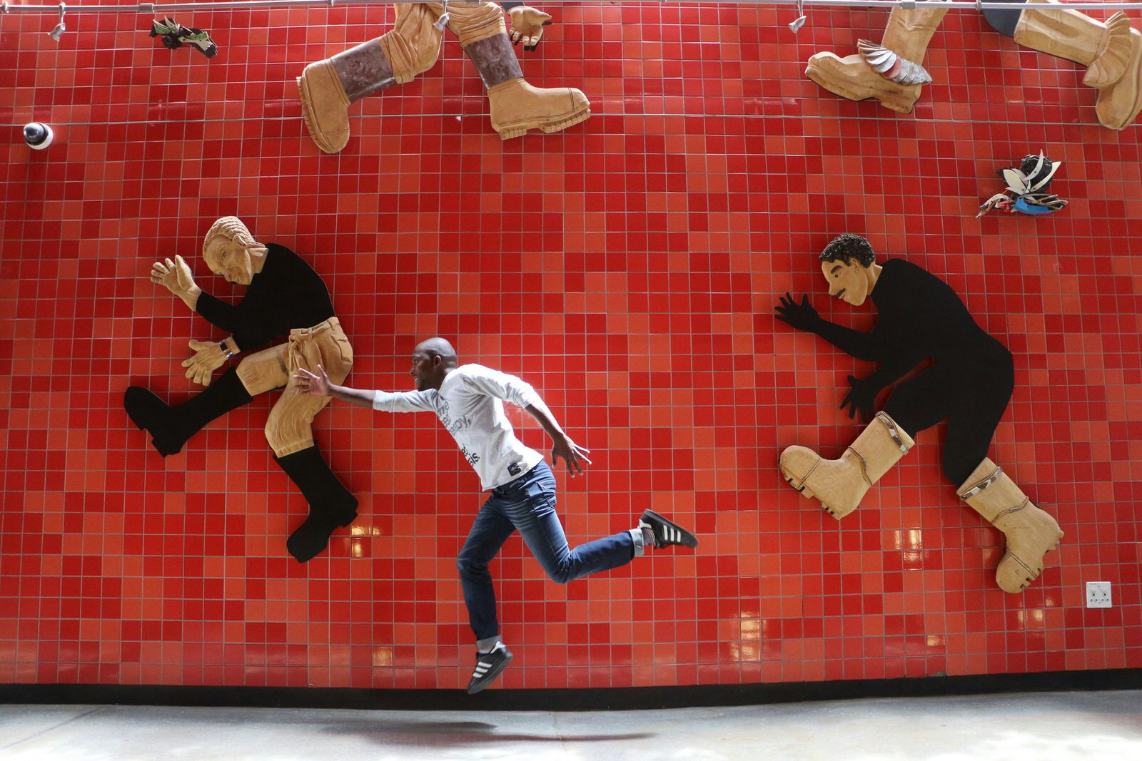 A large red-tiled wall is adorned with simplistic-looking human figures in various jumping positions. In the foreground an actor has been captured leaping in the air in a similar position © Simon Richmond / Lonely Planet