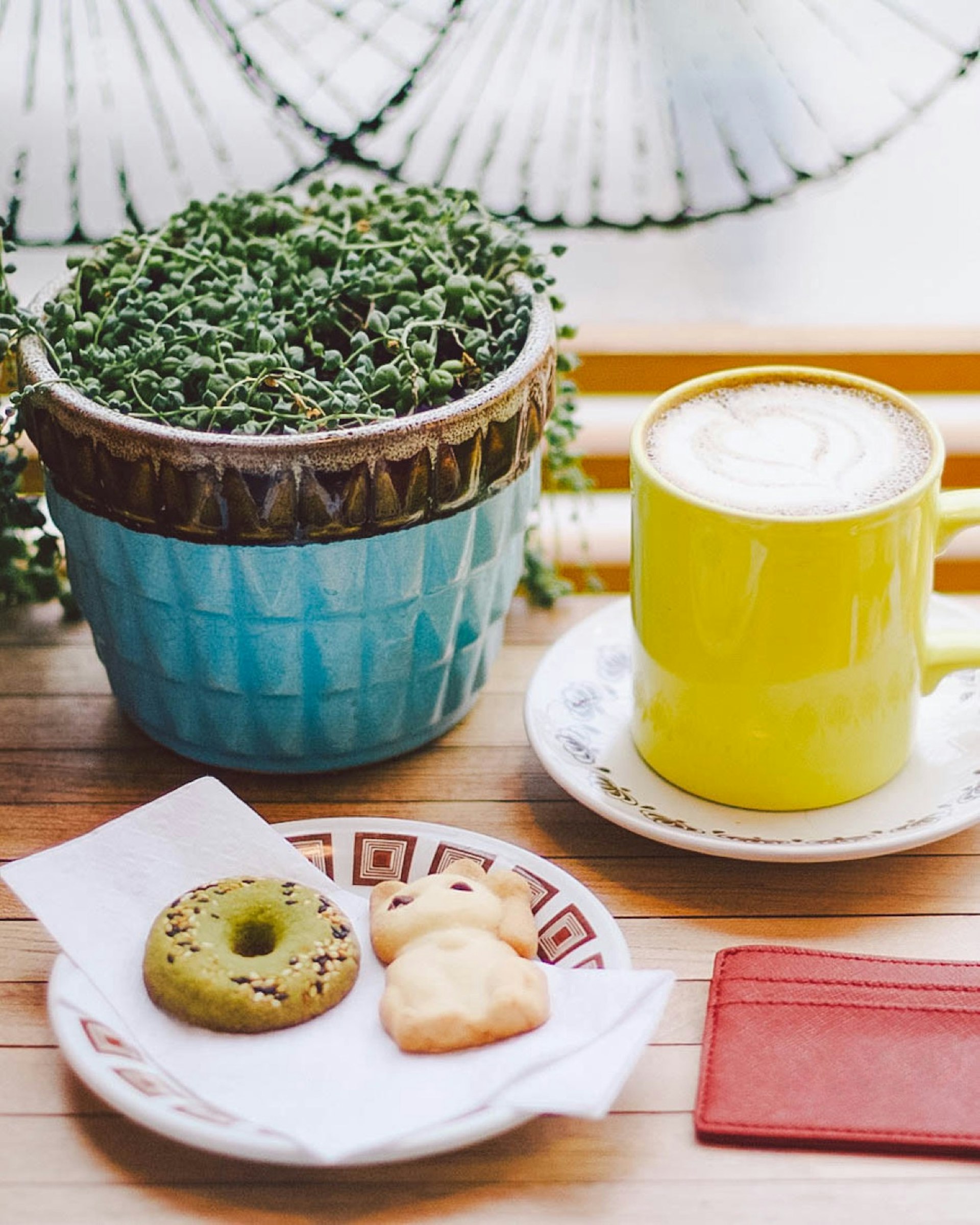 A yellow mug of coffee sits next to a potted plant and a small plate with two cookies on it © Jessica Lam / Lonely Planet