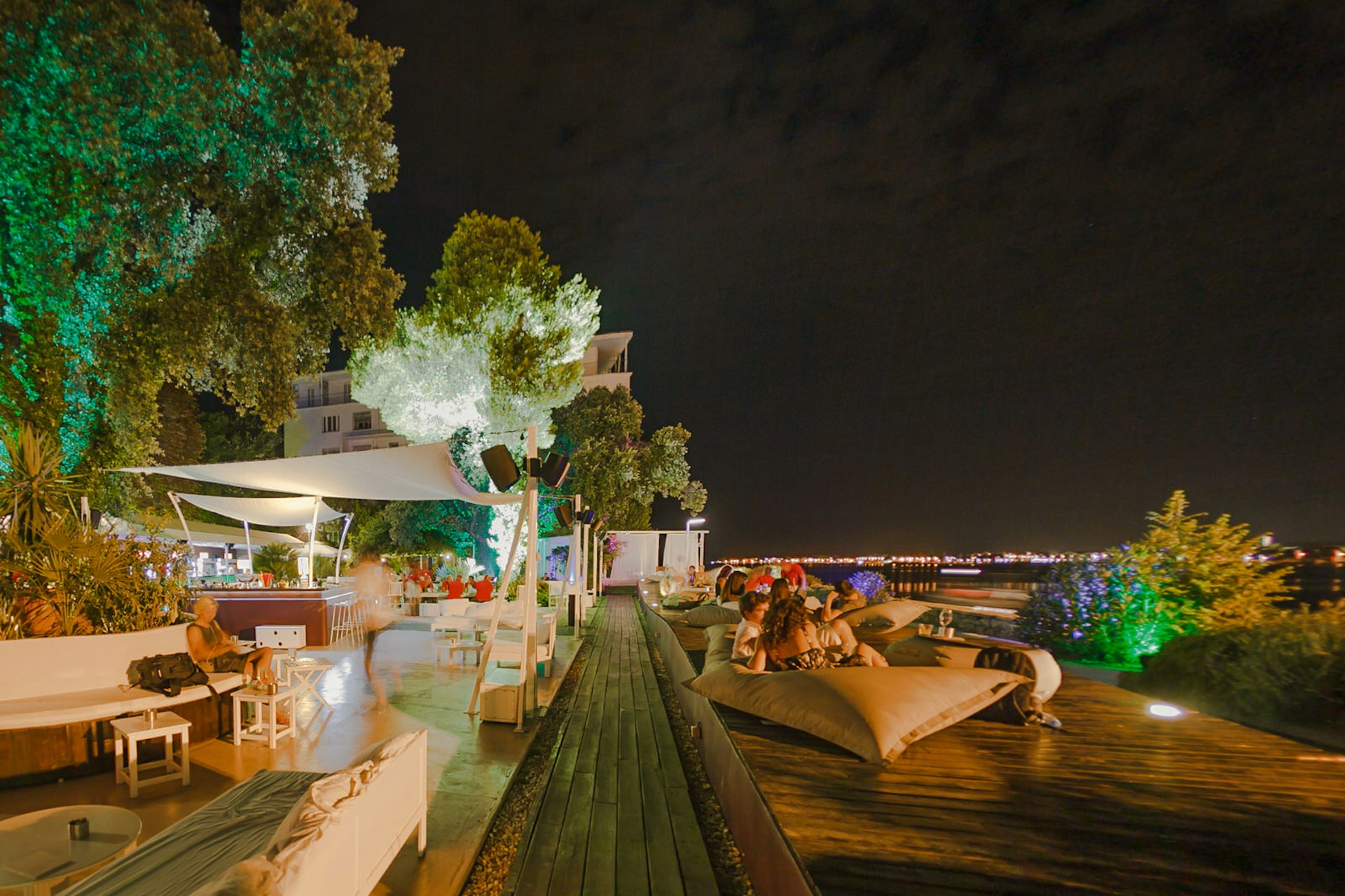 Nighttime shot of people sitting on giant cushions looking out to sea © Tim Ertl / Garden Lounge Zadar