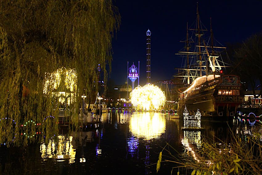 Tivoli at night, with colourfully-illuminated buildings and a water and light show © Caroline Hadamitzky / Lonely Planet