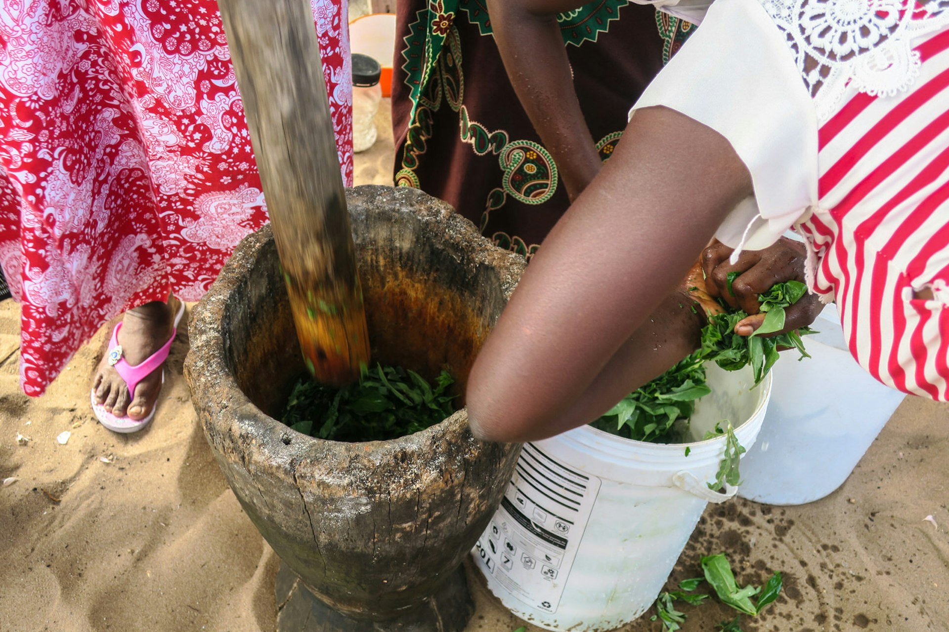 This images looks down the length of a long wooden pestle into the mortar filled with cassava leaves © Melissa Hobson / Lonely Planet