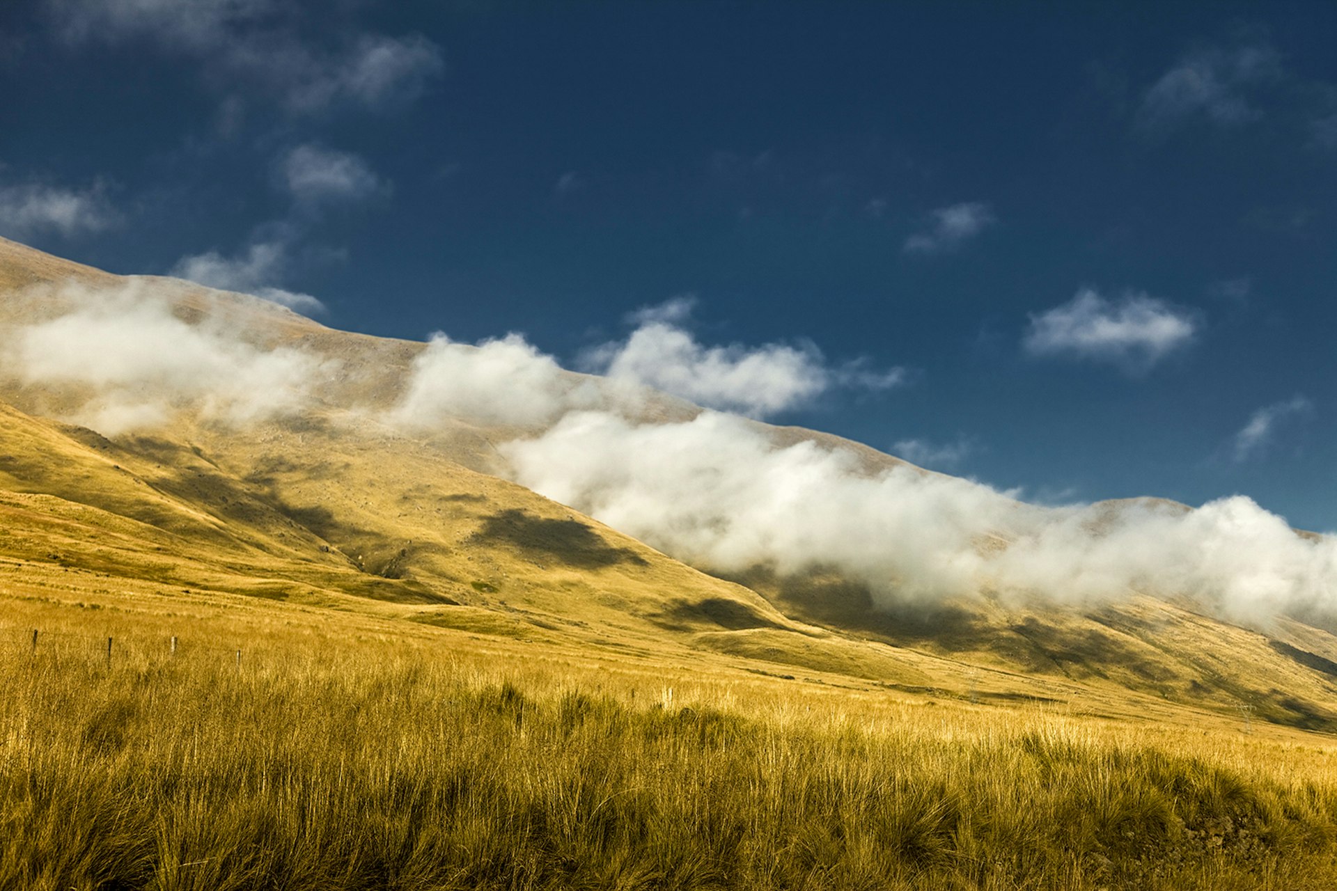 A grassy hillside with clouds against a blue sky in Argentina © Picturegarden / Getty Images