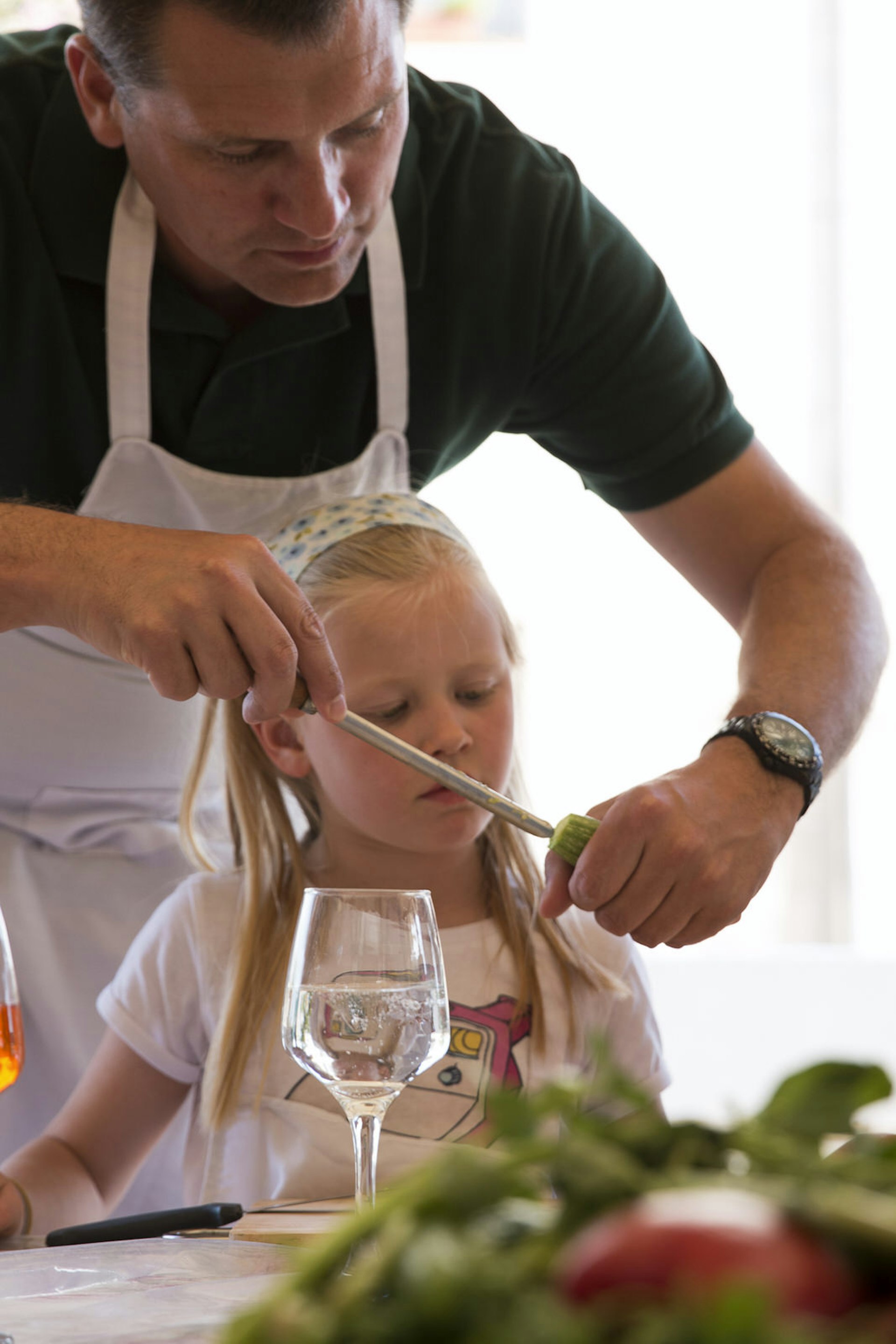 A man in an apron shows a young blonde girl a cooking technique © Beit Sitti