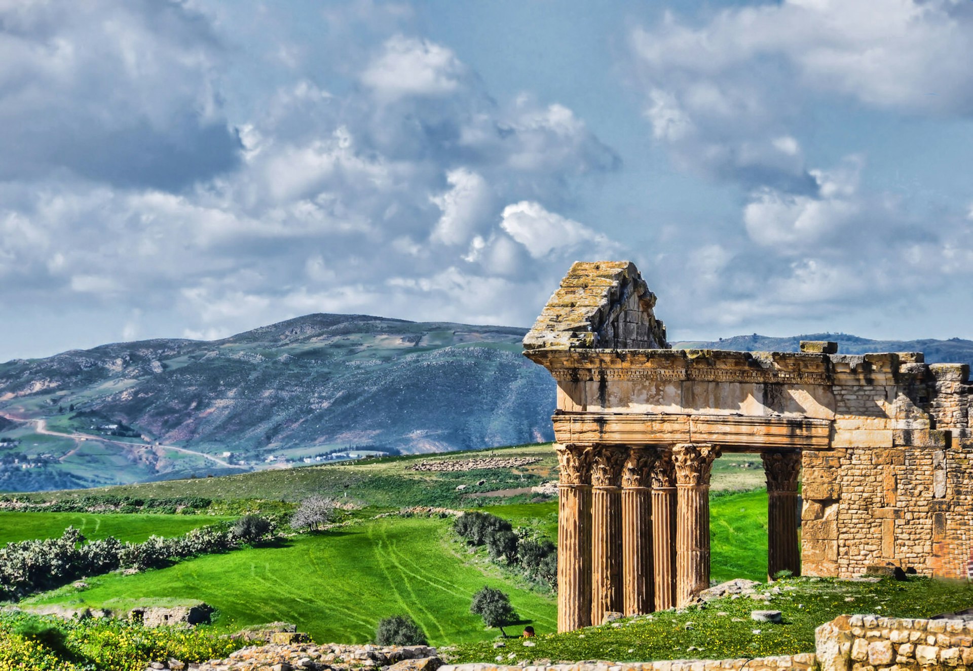 View of the Roman Temple of Jupiter at the archaeological site of Dougga, with mountains in the background © Rosita So Image / Getty Images