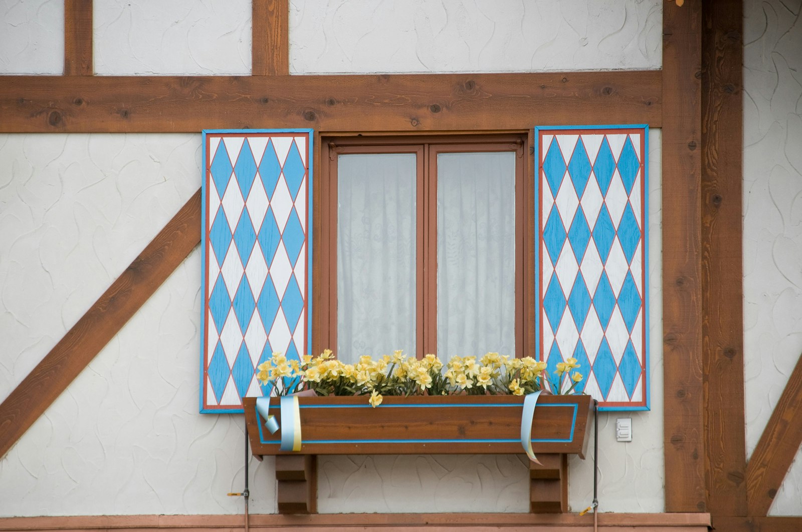 Close up of window with blue-and-white harlequin print shutters and yellow flowers in a windowbox on a beamed, Bavarian-style building in Frankenmuth, Michigan © RiverNorthPhotography / Getty Images