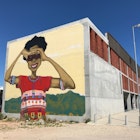 A massive mural of young black South African woman, with her arms raised to shade her eyes from the sun, stares out from the end of the Isivivana Centre's concrete facade © Simon Richmond / Lonely Planet