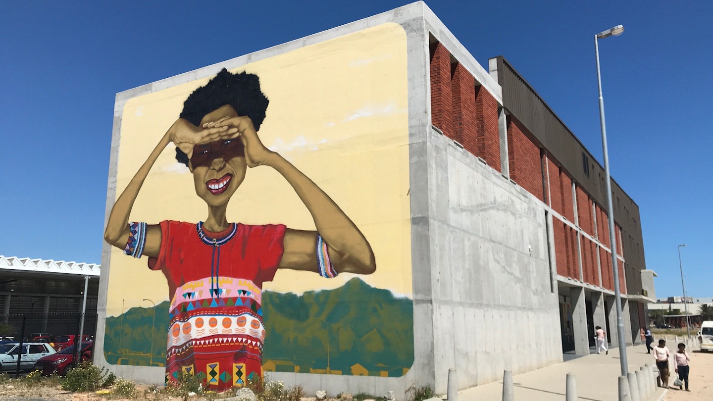 A massive mural of young black South African woman, with her arms raised to shade her eyes from the sun, stares out from the end of the Isivivana Centre's concrete facade © Simon Richmond / Lonely Planet
