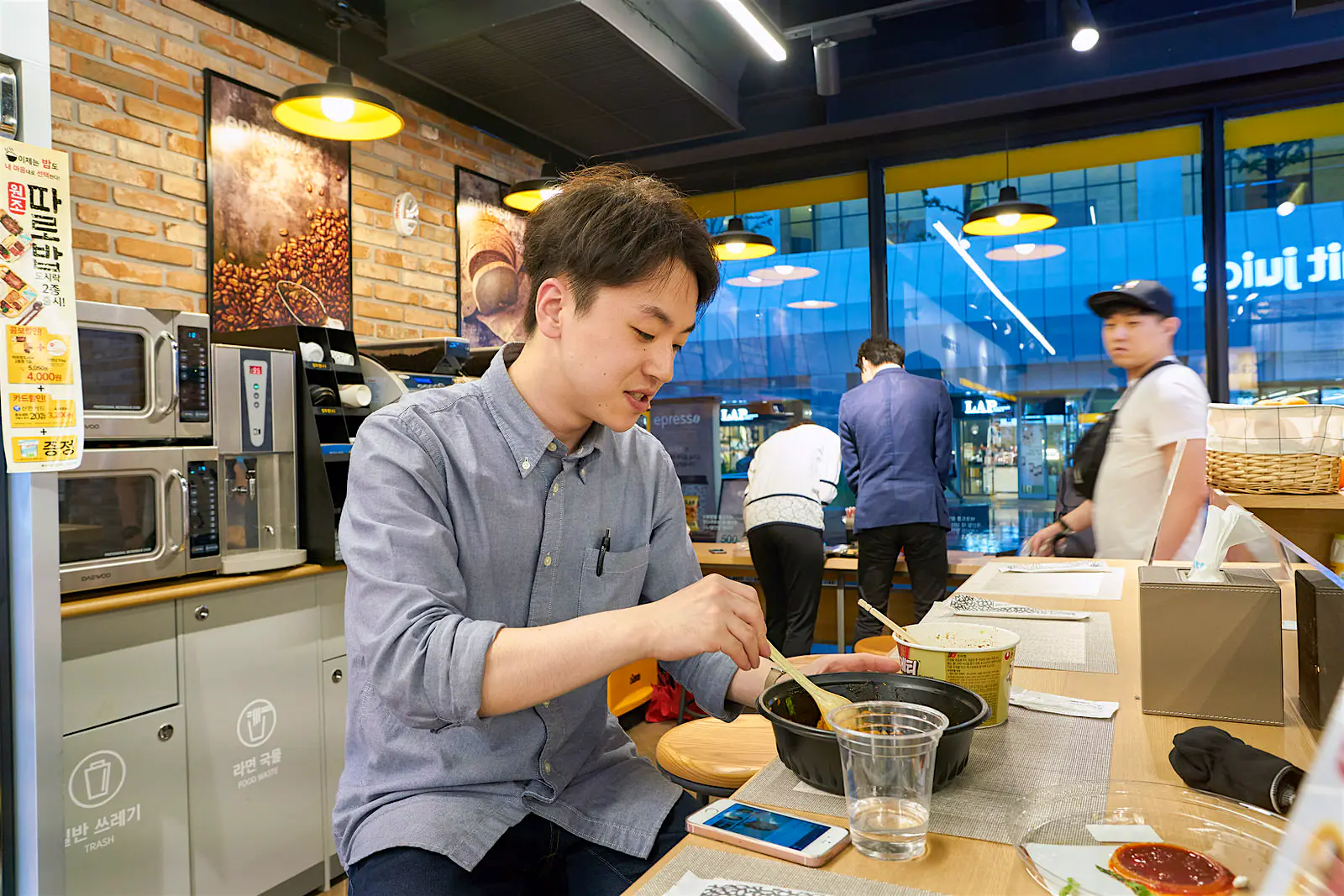 Features - Most convenience stores have a cooking area where you can make elaborate ramen, microwaved meals, coffee and drinks © Sorbis / Shutterstock A man stirs a bowl of instant noodles in a cooking area. Most convenience stores have a cooking area where you can make elaborate ramen, microwaved meals, coffee and drinks © Sorbis / Shutterstock