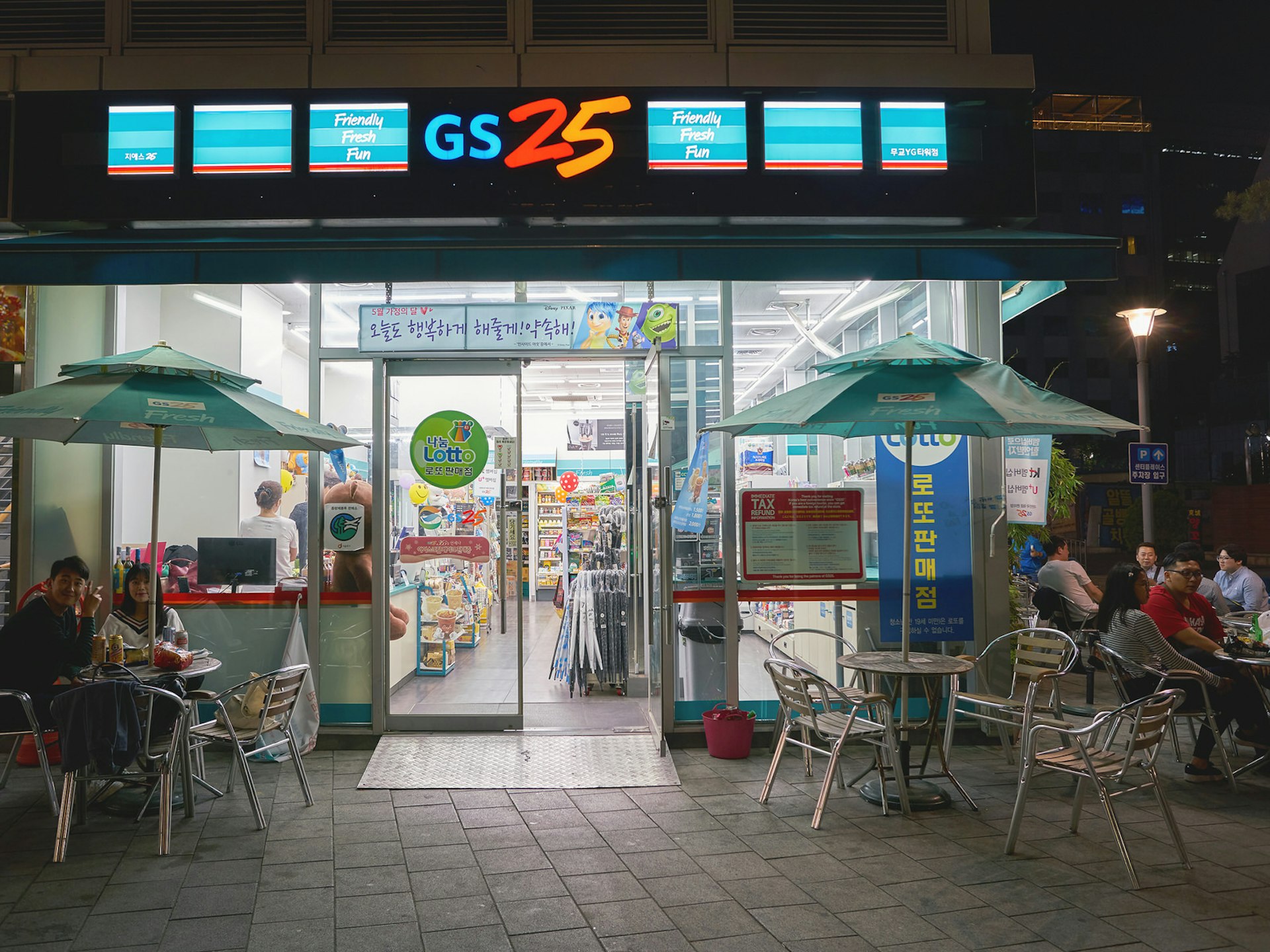 A GS25 convenience store at night, with tables of patrons drinking out front. Most Korean convenience stores have tables for you to linger at, drinking into the night © Sorbis / Shutterstock