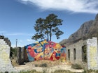 A fantastically bright mural covers one of two remaining stone walls of a ruined home in Kylemore. A large tree climbs into the sky behind it, with the mountains looming in the distance © Simon Richmond / Lonely Planet