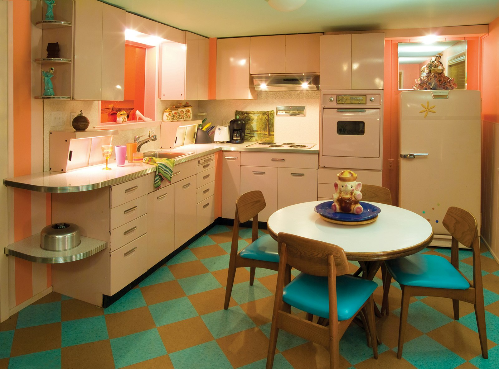 Wide interior shot of turquoise, pink and orange mid-century modern kitchen, with colorful linoleum floor and pale pink cabinets © Lazy Meadow LLC