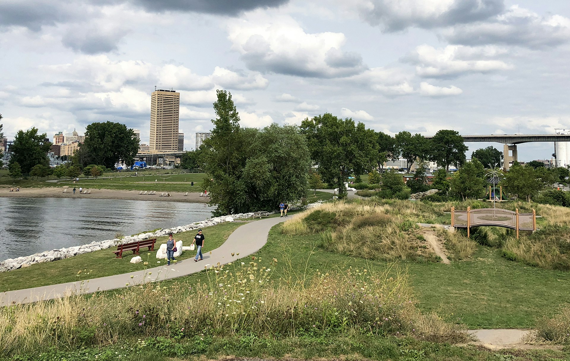 Green grass, sand beach and inlet of Lake Erie on Buffalo's Outer Harbor, with the city and the skyway highway in the background on a summer day