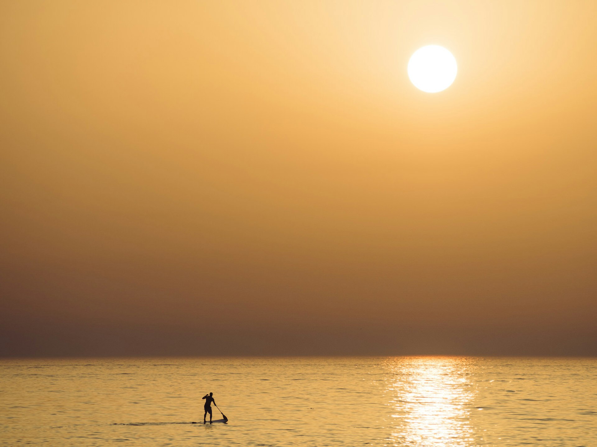 A lone standup paddler in the sea by sunset in Dubai © Miemo Penttinen - miemo.net / Getty Images