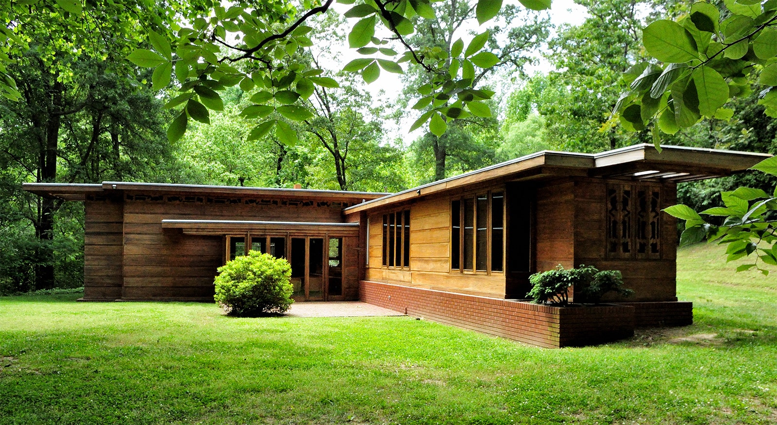 Exterior of one-story wood modernist home in a green yard shaded by trees on a summer day © dw_ross / CC-by-2.0