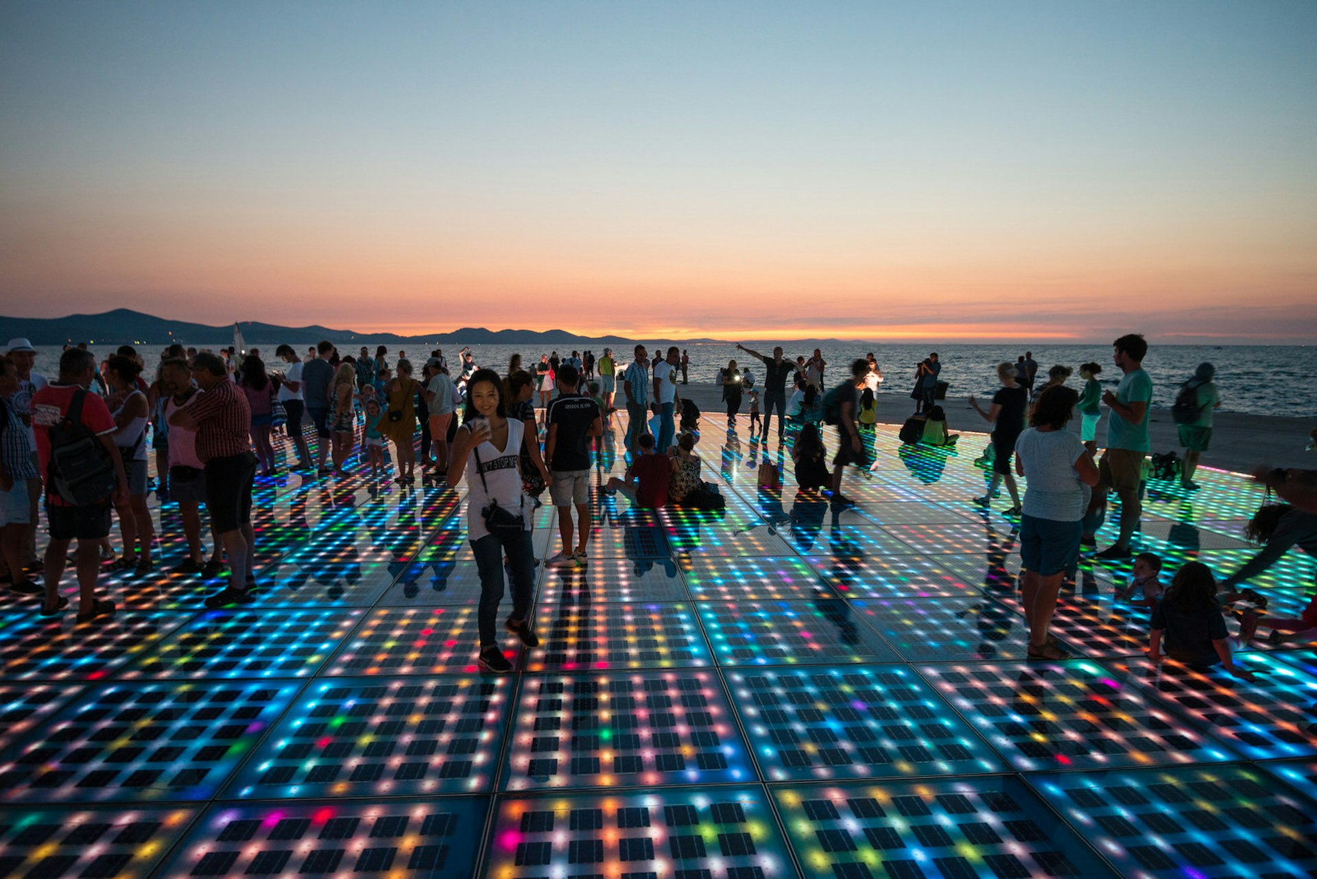 People stand on a platform with hundreds of multicoloured lights as the sun sets © Ventura / Shutterstock