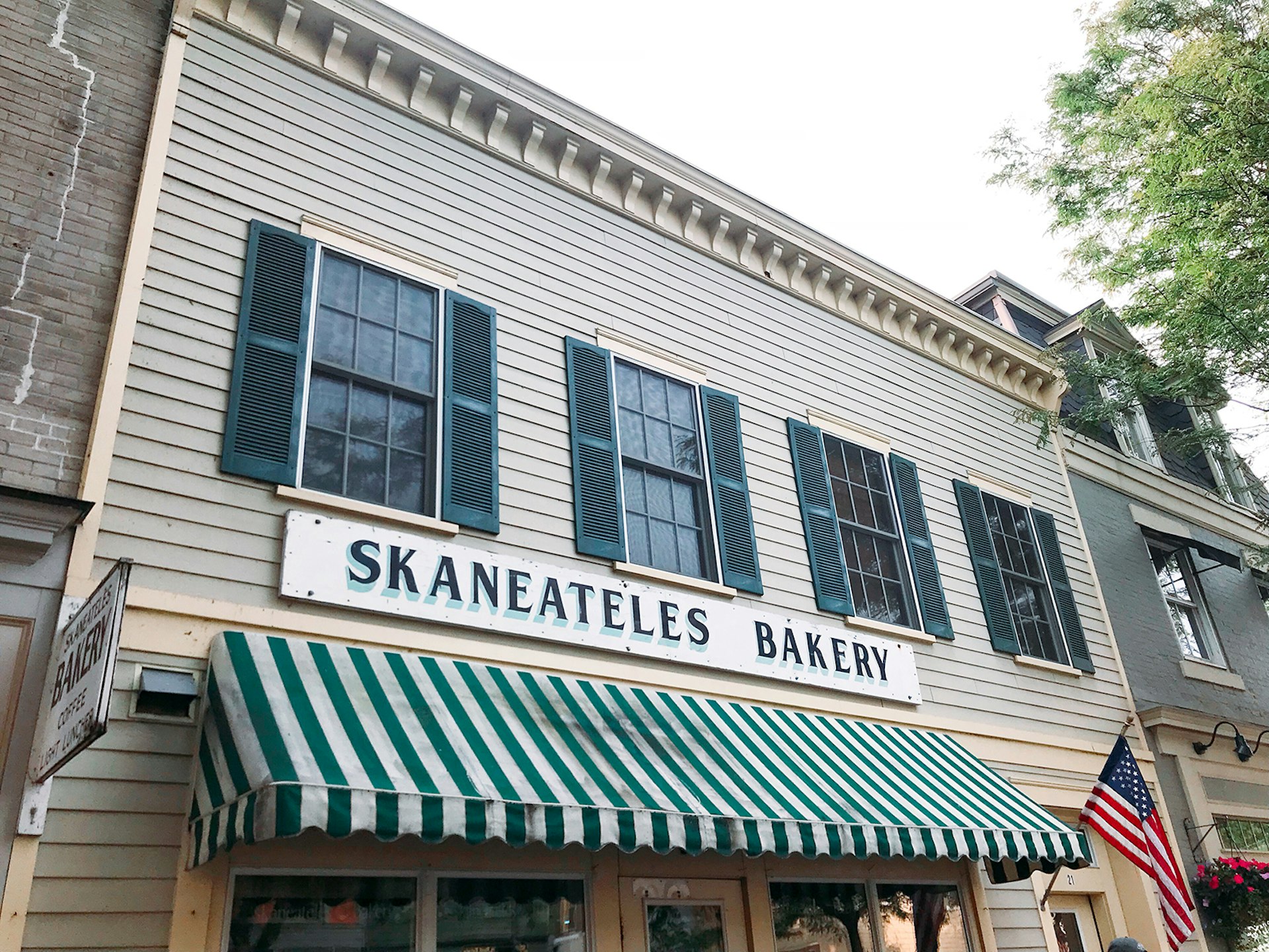 Close-up of facade of Skaneatles Bakery, a 19th-century building with green shutters and a green-and-white striped awning © Mikki Brammer / Lonely Planet