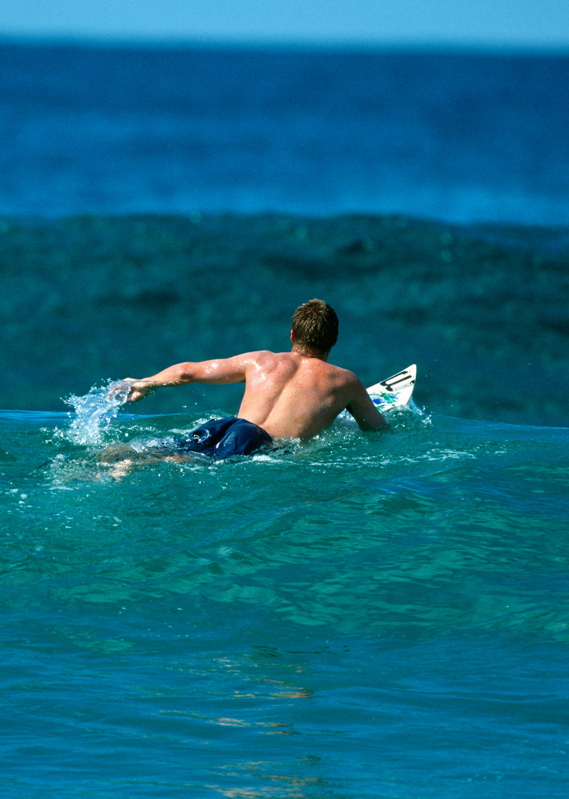 A surfer paddles away from the beach and into an oncoming set of waves © Chris van Lennep / Getty Images