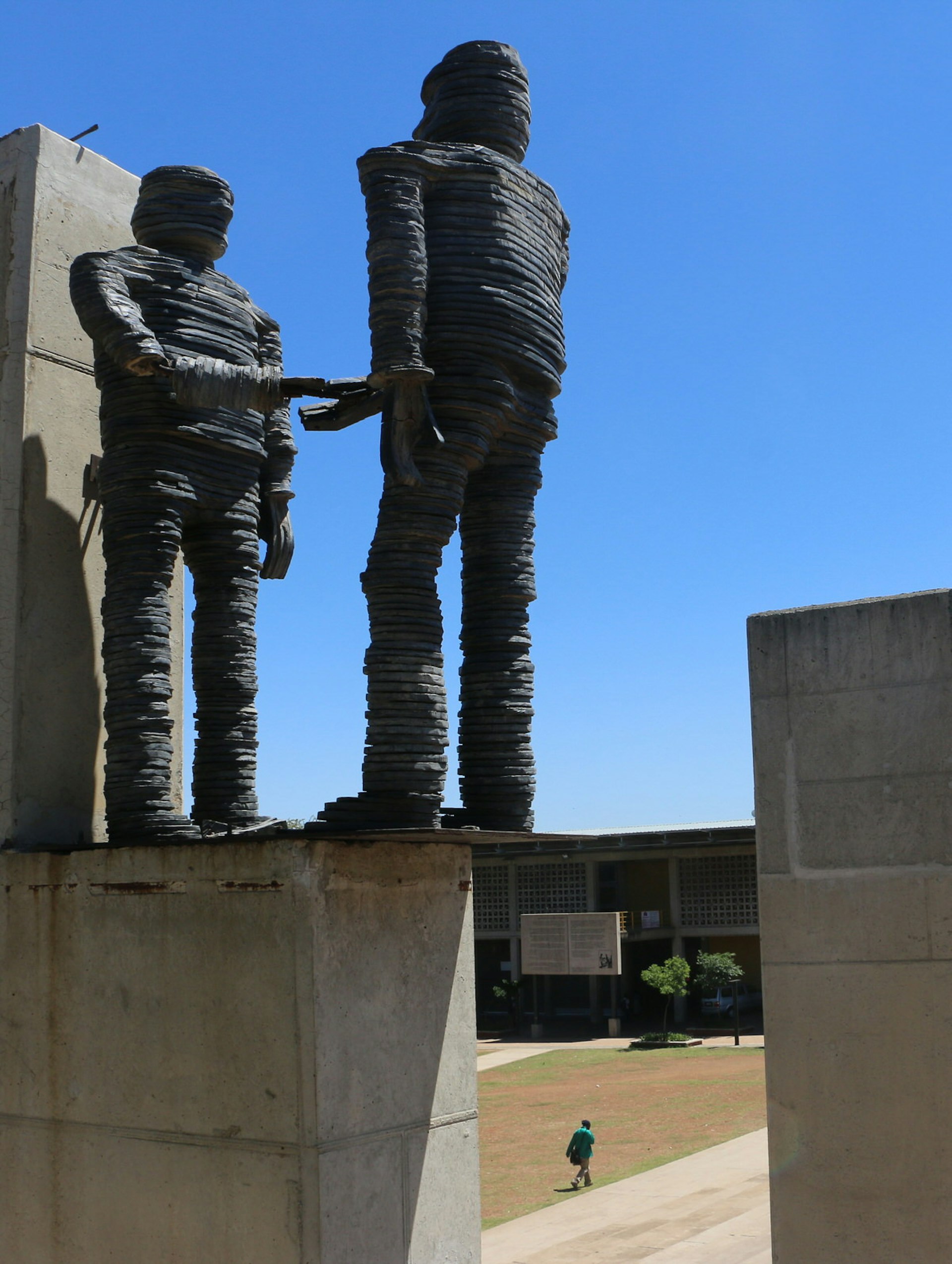 Two massive figures stand atop a concrete plinth, each extending an arm out for a handshake. The square stands below them, with the whole scene covered with a brilliant blue sky © Simon Richmond / Lonely Planet