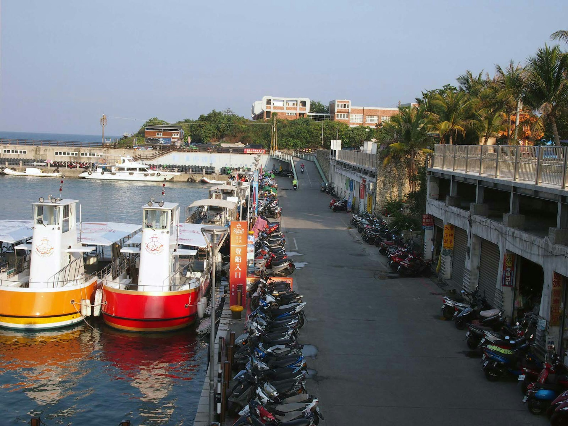 A view of the harbour with docked boats and scooters parked along the waterside. It's easy to hire scooters to get around Little Liuchiu © Tess Humphrys / Lonely Planet