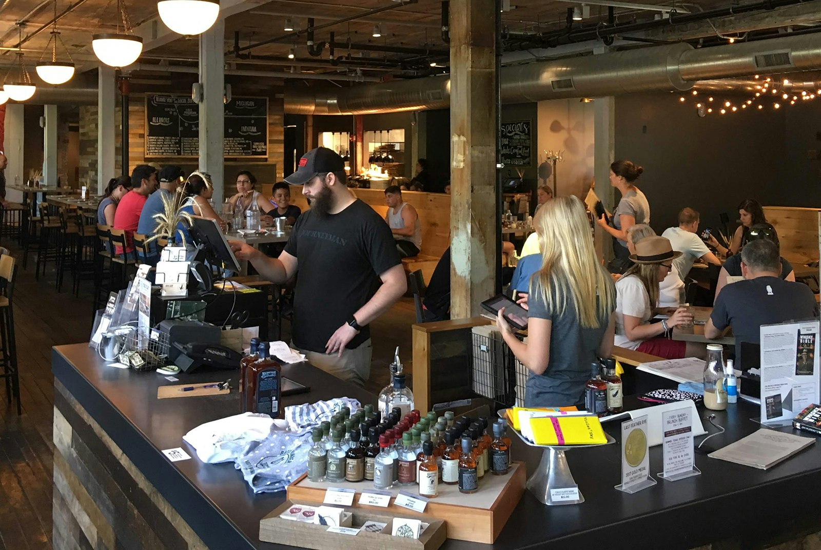 A man and a woman stand behind a counter while dozens of people fill booths and tables behind them in an open, high-ceilinged taproom in Harbor Country Michigan
