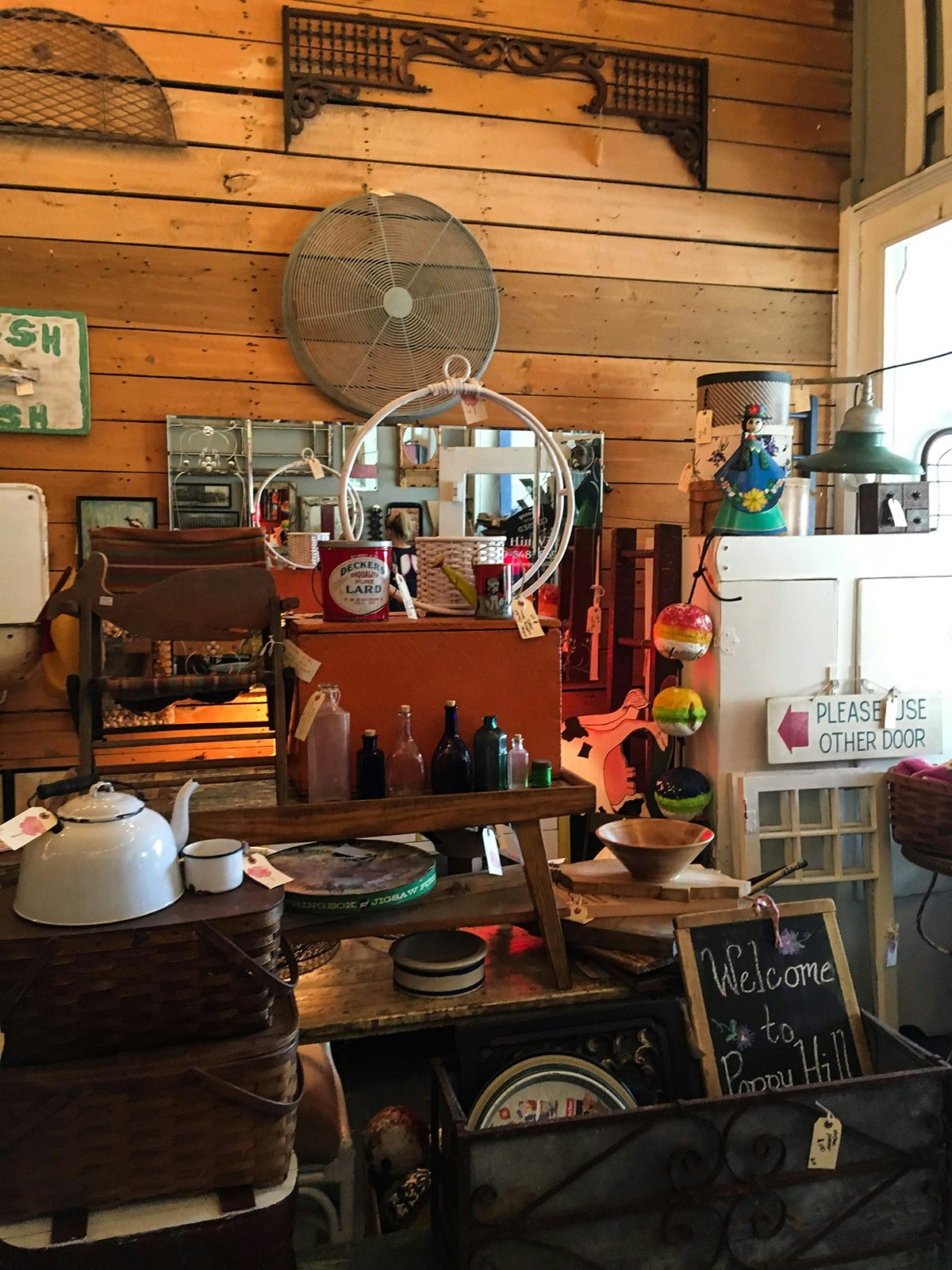 Shop interior in Harbor Country Michigan with a wooden wall filled with vintage housewares, including a white cabinet, an enamel teapot and a huge metal fan