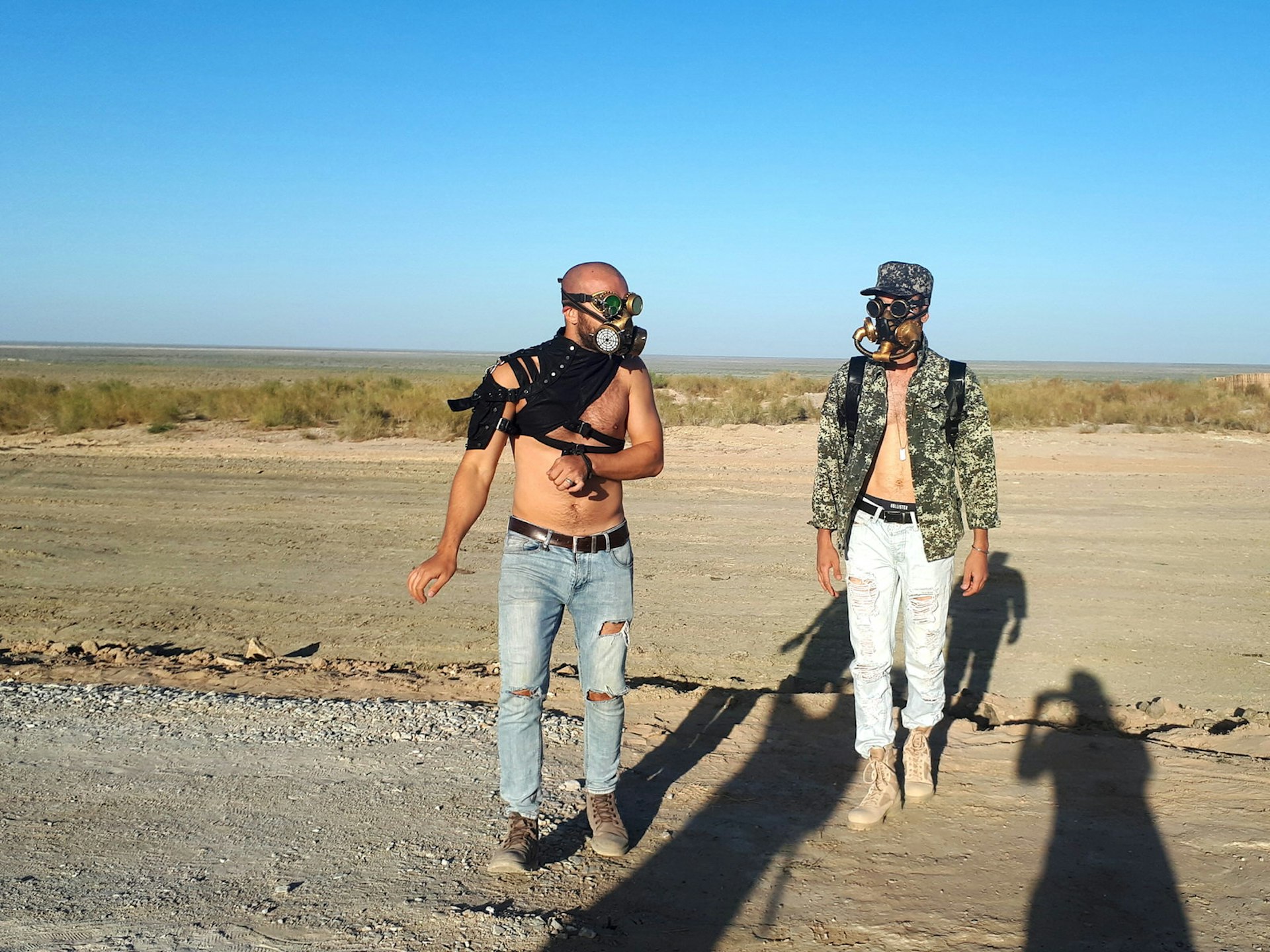 Two men in gas masks and ragged, torn clothing, in the desert