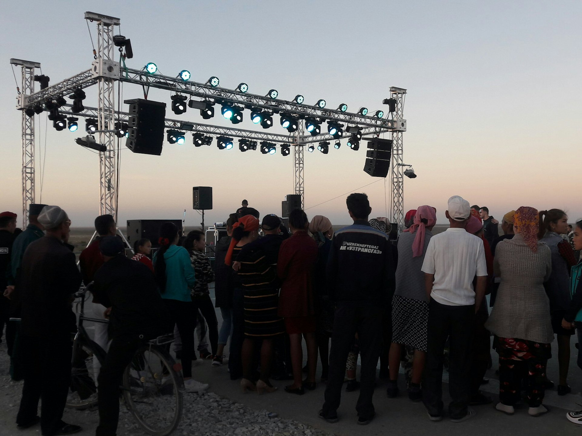 Festival attendees stand near a stage erected in the desert as the sun sets.