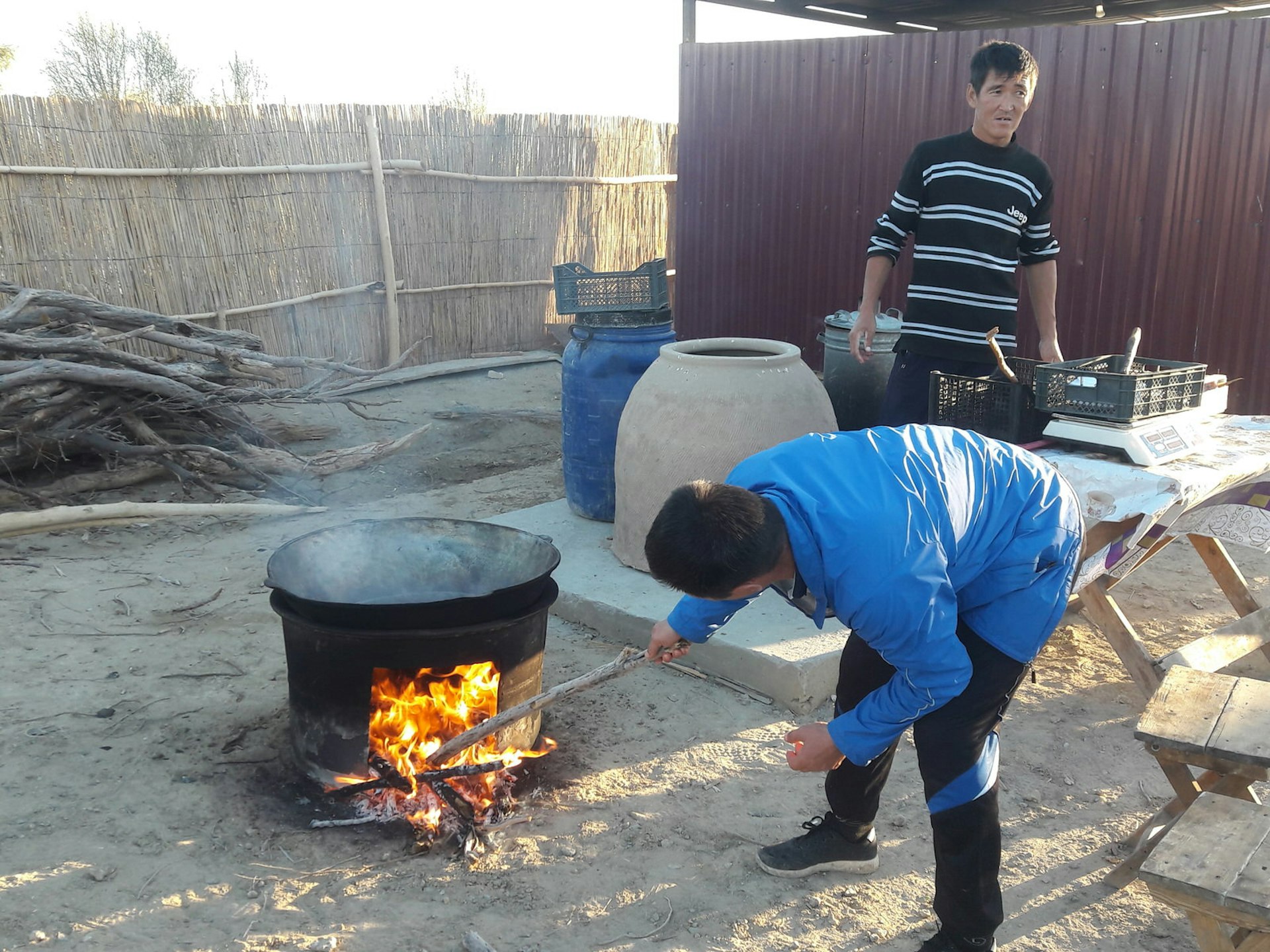 One man putting a stick into a fire under a large pot