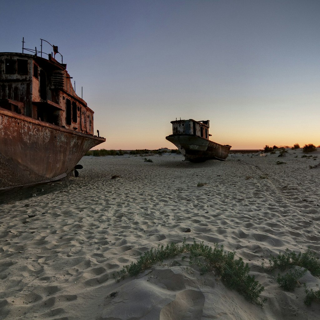 Rusting ships beached on sand with the sunset behind.