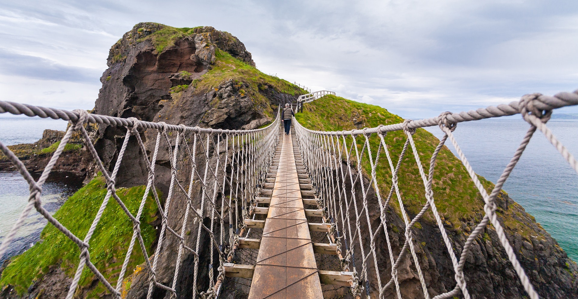 Features - A man crossing the Carrick-a-Rede rope bridge in Antrim, Northern Ireland