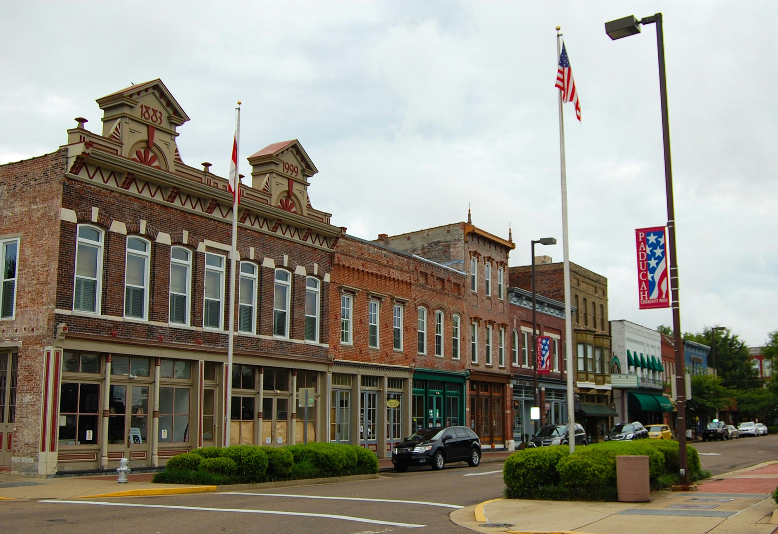 Angle shot of 19th-century commercial brick buildings lining the main street of Paducah, Kentucky, with an American flag in the foreground and clouds overhead