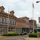 Angle shot of 19th-century commercial brick buildings lining the main street of Paducah, Kentucky, with an American flag in the foreground and clouds overhead