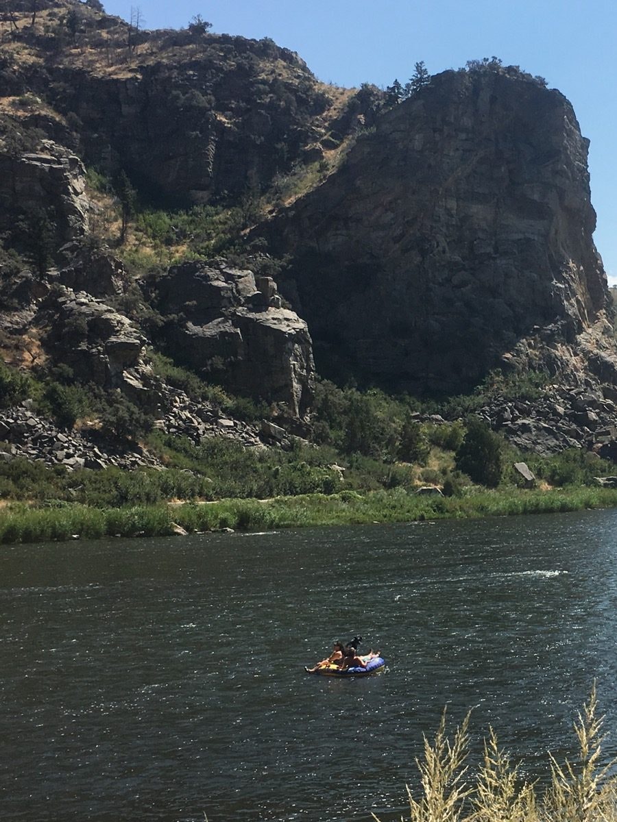 Two people ride inner tubes down a river with a rocky outcrop looming overhead against a brilliant blue sky. © Jay Gentile / Lonely Planet