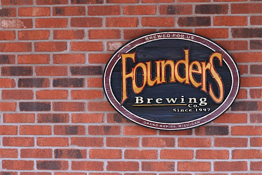 Red brick wall with oval sign containing Founders Brewing Co logo: Yellow curving words in a serif font on a green background. The number of craft breweries continues to grow in the United States. 