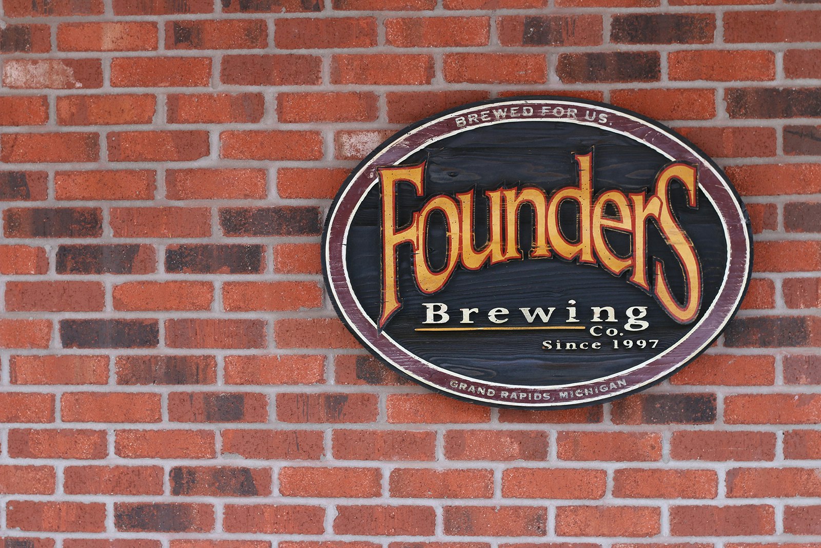 Red brick wall with oval sign containing Founders Brewing Co logo: Yellow curving words in a serif font on a green background. The number of craft breweries continues to grow in the United States. 