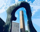 A mid-century modern church bell tower is framed by a blue abstract sculpture by Henry Moore in Columbus Indiana on a sunny day