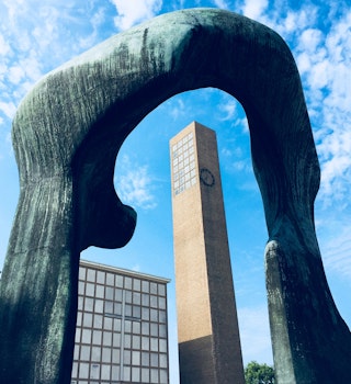 A mid-century modern church bell tower is framed by a blue abstract sculpture by Henry Moore in Columbus Indiana on a sunny day