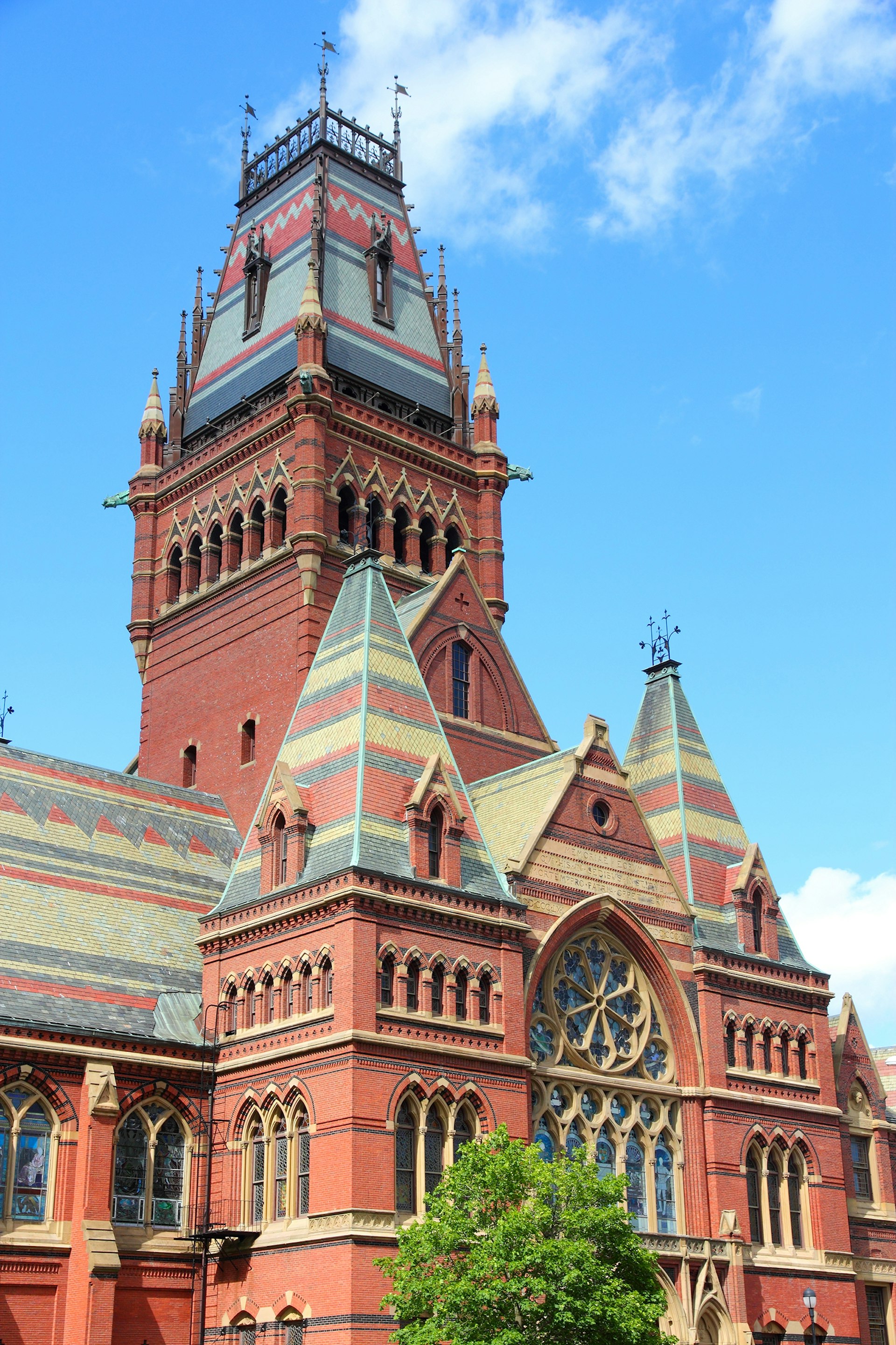 Close up of red brick gothic building with cathedral-like rose window and multicolored roof