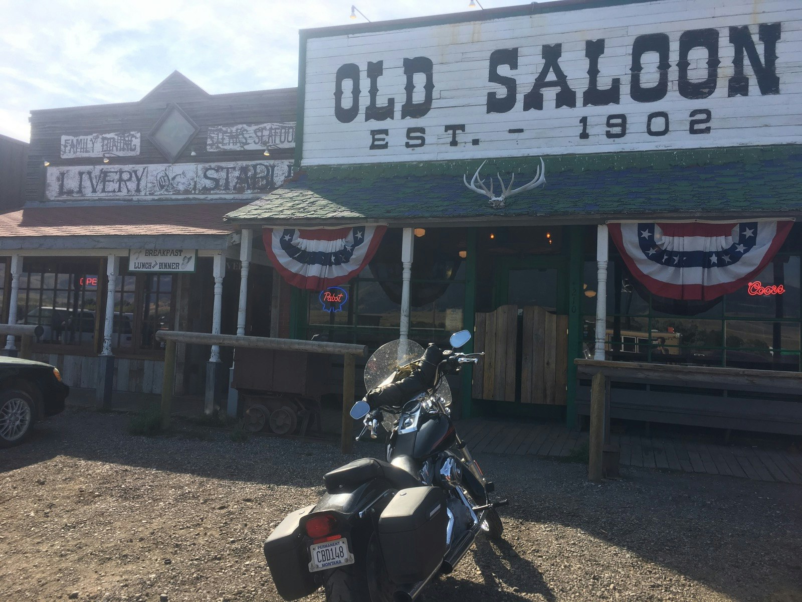 A motorcycle is parked in front of an old-time saloon, complete with bunting and a sign that says it was established in 1902 © Jay Gentile / Lonely Planet