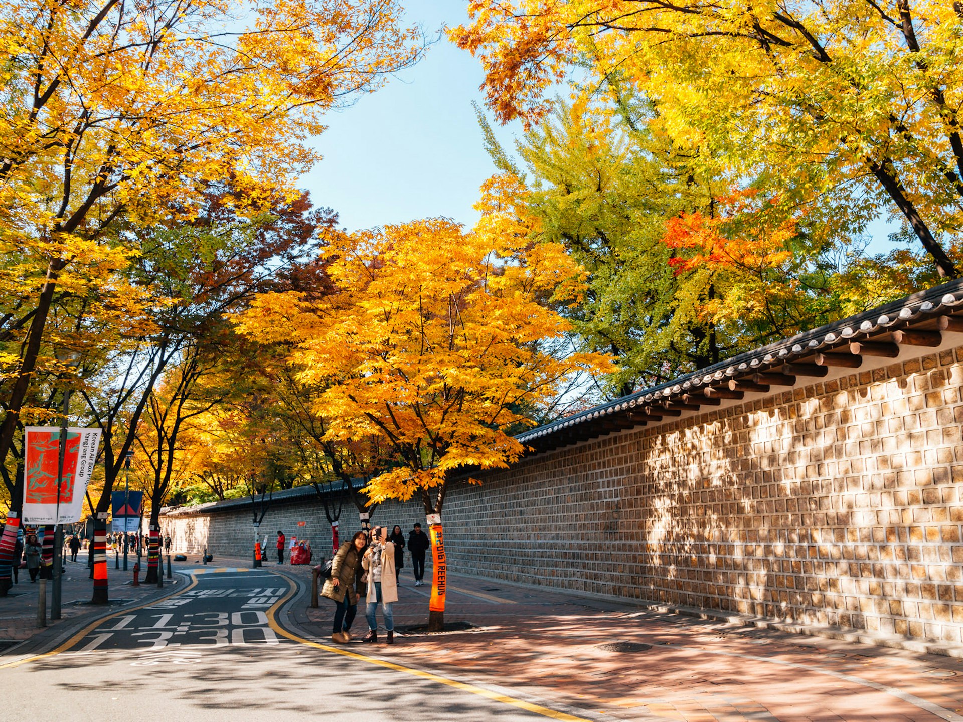 Several walkers take a selfie in front of yellow autumn trees next to a high stone wall