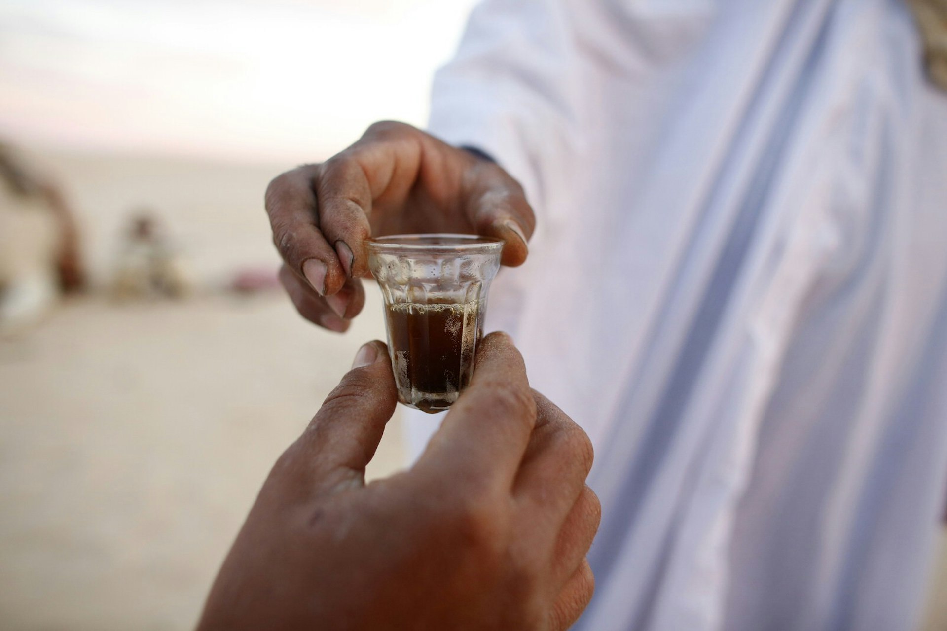 Close up of a small tea glass being passed between two men in the Sahara, Tunisia