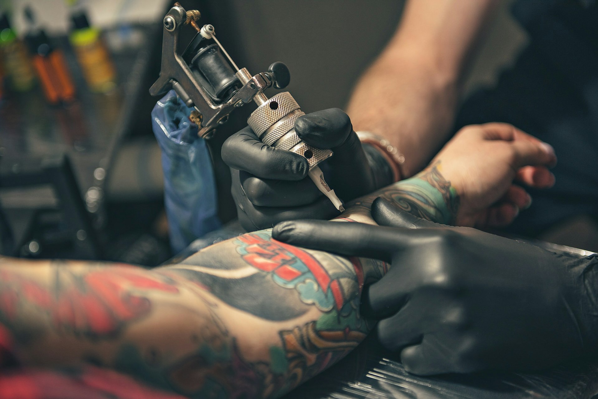 A tattoo artist tattoos a customer's arm